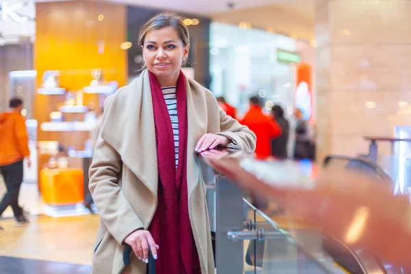 At the mall lifestyle fashion portrait of stunning brunette girl. Walking on At the mall. Going shopping. Wearing stylish white fitted coat, red neckscarf, black umbrella cane. Business woman.