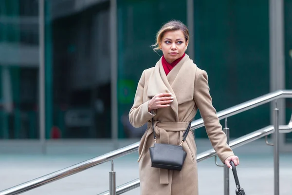 Estilo de vida ao ar livre retrato de moda da menina morena deslumbrante. Caminhando na rua da cidade. Vou às compras. Vestindo elegante casaco branco equipado, lenço de pescoço vermelho, bengala guarda-chuva preto. Mulher de negócios. Preto. — Fotografia de Stock