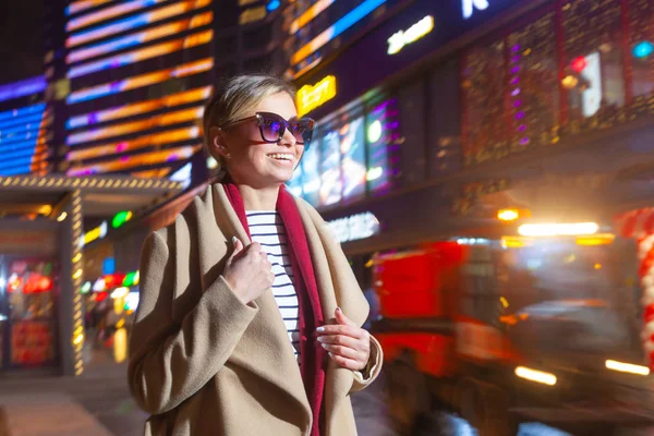 Χαρούμενο κορίτσι με μοντέρνα ρούχα ενθουσιασμένος με φώτα νύχτα σε Big City, όμορφη μελαχρινή γυναίκα σε γυαλιά ευτυχής για να περάσετε το βράδυ ελεύθερο χρόνο στο κέντρο της πόλης με φωτισμό νέον. — Φωτογραφία Αρχείου
