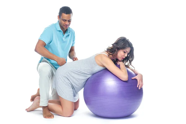 A young black man helps his white wife with birth pain with a ball. Partnered birth, partnered delivery. Isolated white background. — Stock Photo, Image