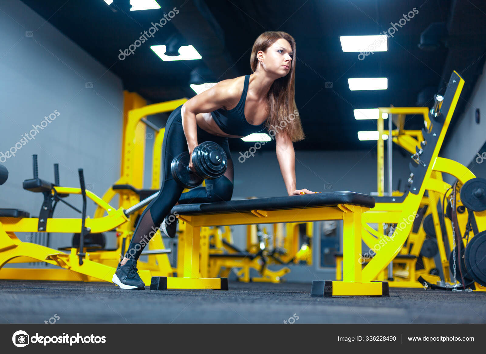 Fitness woman doing exercise with dumbbell leaning on sports bench in a modern gym. — Stock