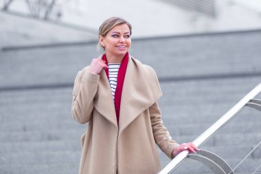 Çekici esmer kızın alışveriş merkezindeki moda portresi. Alışveriş merkezinde yürüyorum. Alışverişe. Şık, beyaz bir ceket ve kırmızı bir eşarp giyiyor. İş kadını. Siyah çanta..