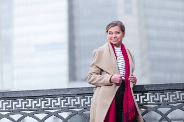 Açık havada yaşayan esmer bir kızın moda portresi. Şehir caddesinde yürüyorum. Alışverişe. Şık, beyaz montlu, kırmızı yakalı, siyah şemsiyeli bir baston giyiyor. İş kadını.