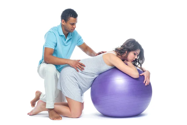 A young black man helps his white wife with birth pain with a ball. Partnered birth, partnered delivery. Isolated white background. — Stock Photo, Image