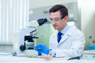 Bilim adamı bir tıp laboratuarında mikroskop ve laboratuvar ekipmanları kullanarak Omega 3 yağ asitlerinin özelliklerini ve faydalarını araştırıyor.
