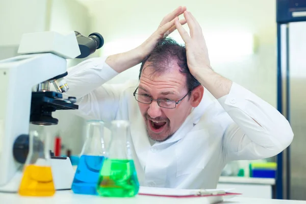 Deli bir kimyager. Çılgın bir bilim adamı bilimsel bir laboratuvarda deneyler yapıyor. Şaşırmış gözlerle şişedeki sıvıyı inceliyor. Saçlarını yoluyor.. — Stok fotoğraf