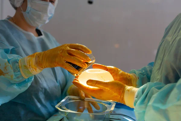 Hôpital. Le chirurgien opère dans la salle d'opération. Le médecin et l'infirmière désinfectent l'implant avant de l'insérer pendant la chirurgie d'augmentation mammaire . — Photo