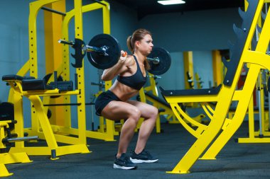 Spor salonunda halter çökerken genç bir fitness kadınının yan görüntüsü..