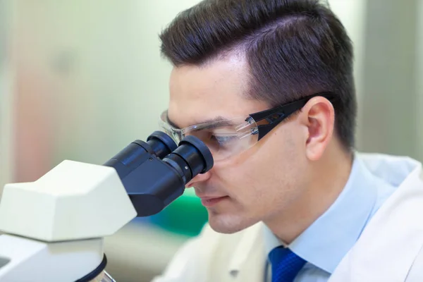 Científico lleva a cabo investigación científica mirando a través del microscopio en un laboratorio médico . —  Fotos de Stock