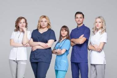 Tıbbi doktorlar başarılı takım gri arka planda ayakta iken kamera bakıyor