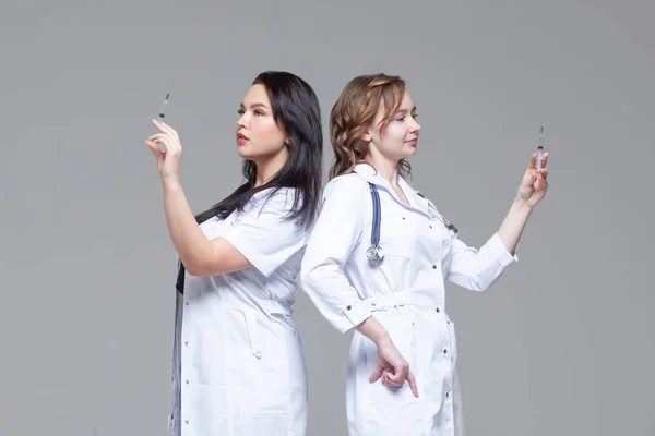Dwie kobiece lekarze stojący z powrotem do tyłu trzymać strzykawki gotowe do wstrzyknięcia — Zdjęcie stockowe