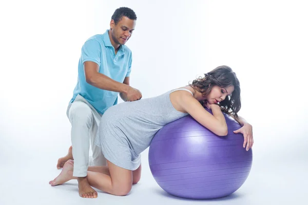 A young black man helps his white wife with birth pain with a ball. Partnered birth, partnered delivery. Isolated white background. — Stock Photo, Image