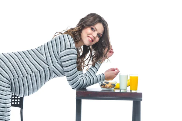 Młoda kobieta w ciąży siedzi przy stole, na którym znajduje się banan, jest talerz z zbożem, szklanką z kefiru i sokiem. Koncepcja żywienia w czasie ciąży. Izolowane na białym tle. — Zdjęcie stockowe