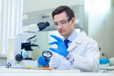 Bilim adamı bir tıp laboratuarında mikroskop ve laboratuvar ekipmanları kullanarak Omega 3 yağ asitlerinin özelliklerini ve faydalarını araştırıyor.