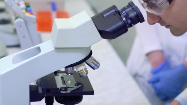 Cientista realiza pesquisa científica olhando através de microscópio em um laboratório médico . — Vídeo de Stock