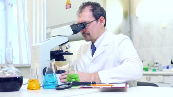 Chemist crazy. A mad scientist conducts experiments in a scientific laboratory. Performs research using a microscope. — Stock Video