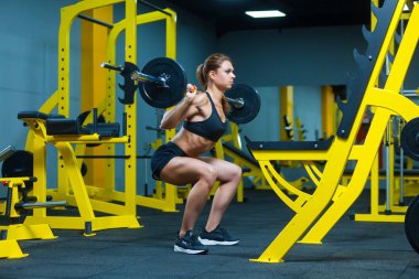 Spor salonunda halter çökerken genç bir fitness kadınının yan görüntüsü..