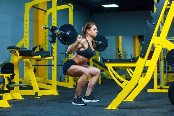 Oldalnézet egy fiatal fitnesz nő csinál súlyzó guggolás egy tornateremben. — Stock Fotó