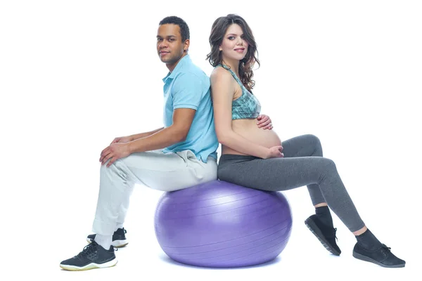Mladý pár a jejich žena v posledních měsících těhotenství sedí na sportovní rohoži nedaleko míče. Černoch a bílá žena. Koncept šťastného páru různých ras připravujících společně — Stock fotografie