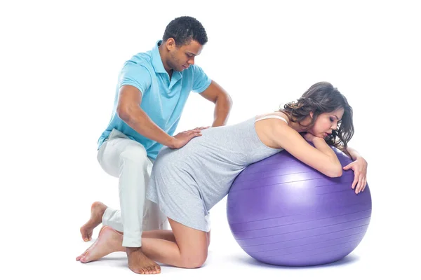 A young black man helps his white wife with birth pain with a ball. Partnered birth, partnered delivery. Isolated white background. — Stock Photo, Image