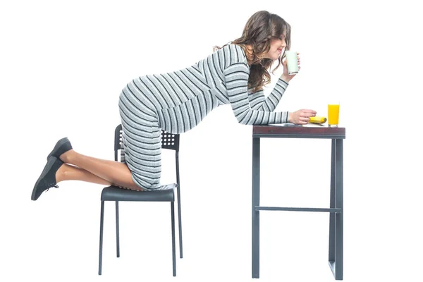 Une jeune femme enceinte s'assied à une table sur laquelle se trouve une banane, il y a une assiette avec des céréales, un verre avec du kéfir et du jus. Le concept de nutrition pendant la grossesse. Isolé sur fond blanc . — Photo