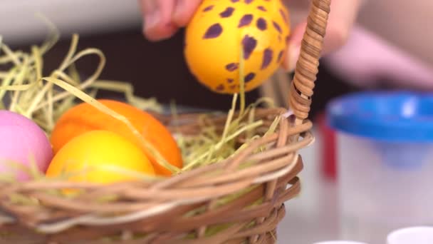 Feliz Pascua. Niña pintando huevos de Pascua. Primer plano de una mano de chicas poniendo un huevo pintado en una canasta. Linda niña pequeña con orejas de conejo en el día de Pascua . — Vídeos de Stock