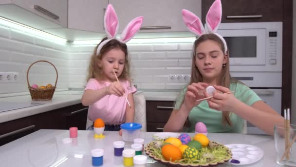 Veselé Velikonoce. Dvě sestry malují velikonoční vajíčka. Šťastné rodinné děti se připravují na Velikonoce. Roztomilé malé dítě dívka nosí králičí uši na velikonoční den. — Stock video