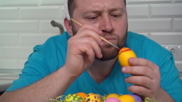 Happy Easter. A man in a rabbit ears blue t-shirt in the kitchen paints eggs preparing for Easter. — Stock Video