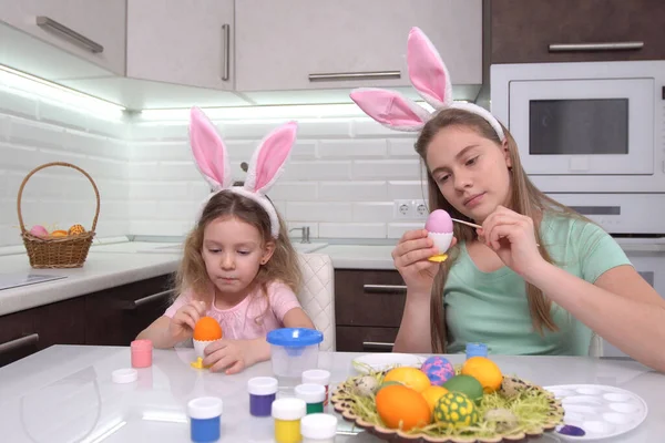 Feliz Pascua. Dos hermanas pintando huevos de Pascua. Felices hijos de familia preparándose para Pascua. Linda niña pequeña con orejas de conejo en el día de Pascua. — Foto de Stock