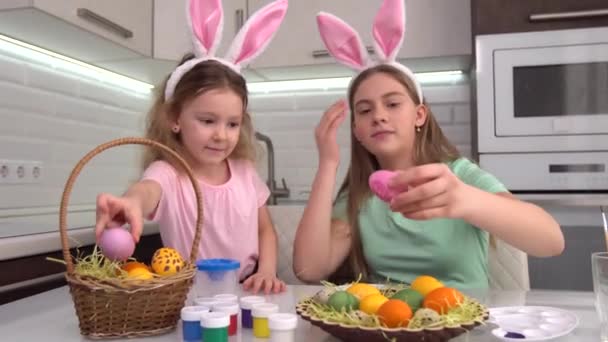 Feliz Pascua. Dos hermanas pintando huevos de Pascua. Felices hijos de familia preparándose para Pascua. Linda niña pequeña con orejas de conejo en el día de Pascua. — Vídeos de Stock