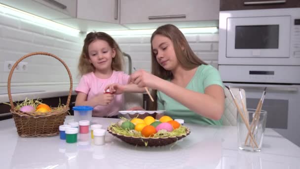 Καλό Πάσχα. Δύο αδερφές βάφουν πασχαλινά αυγά. Ευτυχισμένα παιδιά της οικογένειας ετοιμάζονται για το Πάσχα. Χαριτωμένο κοριτσάκι που φοράει αυτιά λαγού την ημέρα του Πάσχα. — Αρχείο Βίντεο