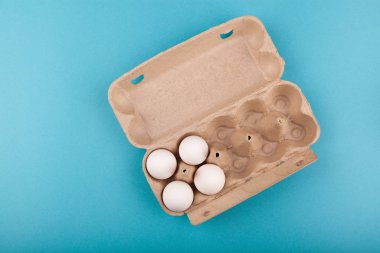 Yumurtalı tavuk yumurtası. Beyaz yumurtalı açık gri bir kutunun üst görüntüsü. Mavi arka planda izole edilmiş. Sağlıklı yaşam tarzı kavramı, saf protein almak. Düzgün bir kahvaltı. Dört yumurta..