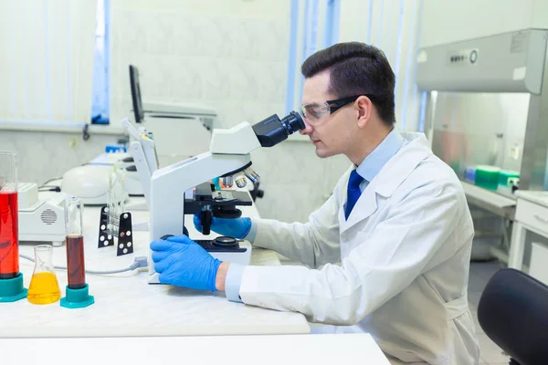 Científico lleva a cabo investigación científica mirando a través del microscopio en un laboratorio médico . —  Fotos de Stock