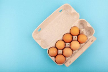 Yumurtalı tavuk yumurtası. Mavi arka planda kahverengi yumurtaları olan açık gri bir kutunun üst görüntüsü. Sağlıklı yaşam tarzı kavramı, saf protein almak. Düzgün bir kahvaltı. Sekiz yumurta..