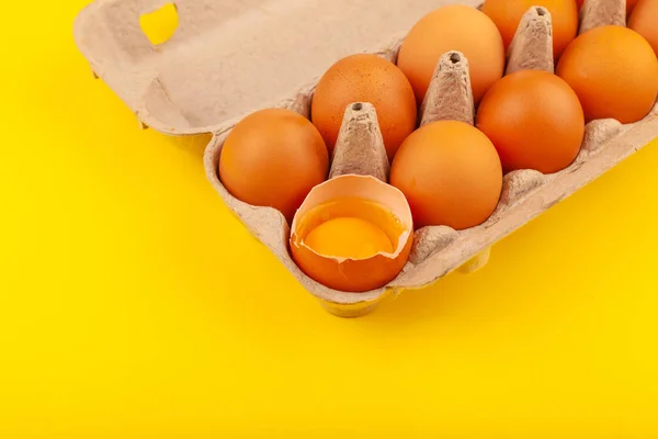 Huevos de pollo. Vista superior de una caja gris abierta con huevos marrones Aislados sobre un fondo amarillo. Un huevo está medio roto, yema redonda amarilla. El concepto de un estilo de vida saludable, obtener proteínas puras — Foto de Stock