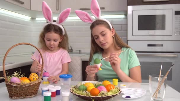Feliz Pascua. Dos hermanas pintando huevos de Pascua. Felices hijos de familia preparándose para Pascua. Linda niña pequeña con orejas de conejo en el día de Pascua. — Vídeos de Stock