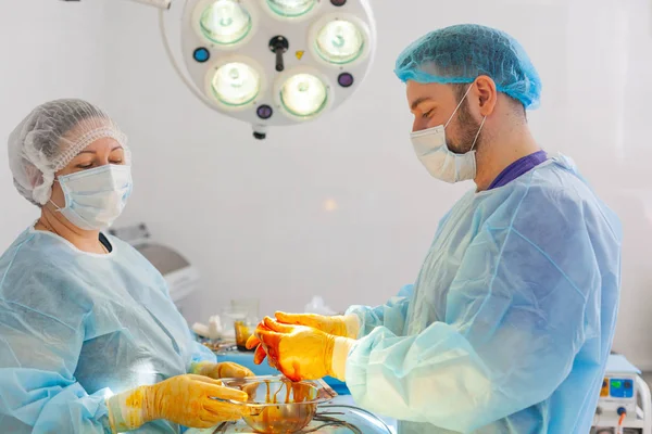 No hospital. O cirurgião opera na sala de operações. O médico e enfermeiro desinfetam o implante antes de inseri-lo durante a cirurgia de aumento da mama . — Fotografia de Stock