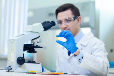 Bilim adamı bir tıp laboratuarında mikroskop ve laboratuvar ekipmanları kullanarak Omega 3 yağ asitlerinin özelliklerini ve faydalarını araştırıyor.