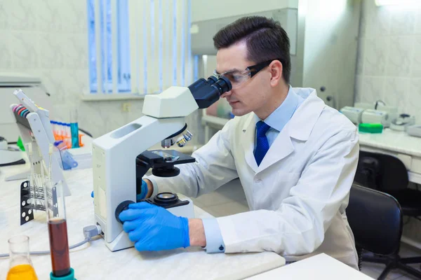 Científico lleva a cabo investigación científica mirando a través del microscopio en un laboratorio médico . —  Fotos de Stock