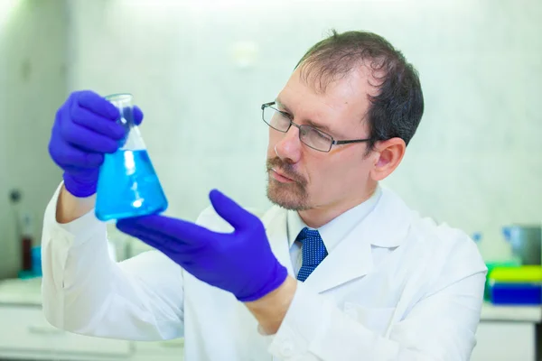 Un científico sostiene y estudia un frasco con líquido azul en un laboratorio científico —  Fotos de Stock