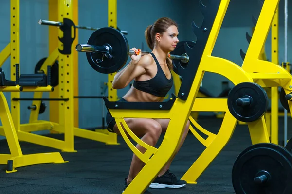 Sidovy av en ung fitness kvinna som gör skivstång knäböj i ett gym. — Stockfoto