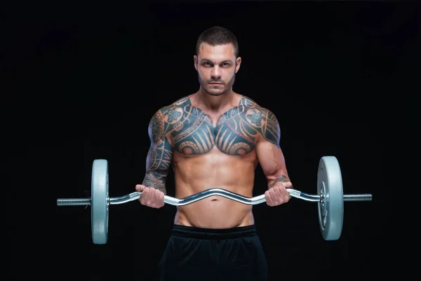 Getatoeëerde sterke gespierde atletische man pompen spieren met lange halter op zwarte achtergrond — Stockfoto