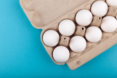 Yumurtalı tavuk yumurtası. Beyaz yumurtalı açık gri bir kutunun üst görüntüsü. Mavi arka planda izole edilmiş. Sağlıklı yaşam tarzı kavramı, saf protein almak. Düzgün bir kahvaltı..