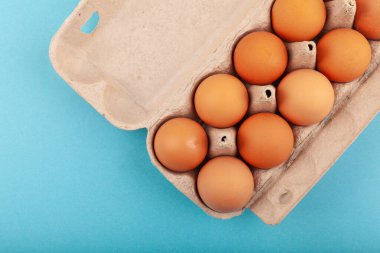 Yumurtalı tavuk yumurtası. Mavi arka planda kahverengi yumurtaları olan açık gri bir kutunun üst görüntüsü. Sağlıklı yaşam tarzı kavramı, saf protein almak. Düzgün bir kahvaltı. Dissati yumurtaları.