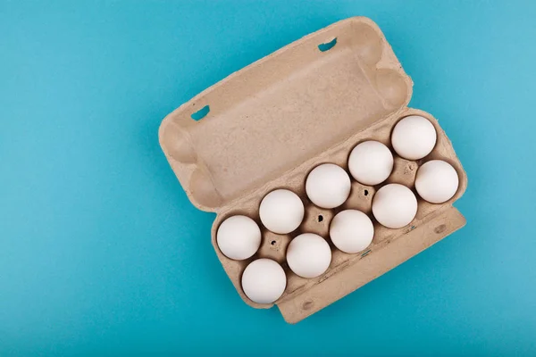 Huevos de pollo. Vista superior de una caja gris abierta con huevos blancos. Aislado sobre un fondo azul. El concepto de un estilo de vida saludable, obtener proteínas puras. Desayuno adecuado . — Foto de Stock