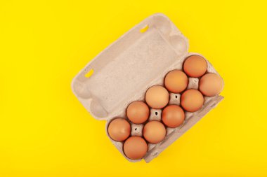 Yumurtalı tavuk yumurtası. Sarı arka planda kahverengi yumurtaları olan açık gri bir kutunun üst görüntüsü. Sağlıklı yaşam tarzı kavramı, saf protein almak. Düzgün bir kahvaltı.. .
