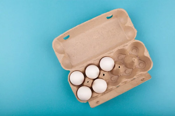 Huevos de pollo. Vista superior de una caja gris abierta con huevos blancos. Aislado sobre un fondo azul. El concepto de un estilo de vida saludable, obtener proteínas puras. Desayuno apropiado. Cinco huevos . — Foto de Stock