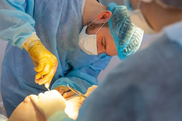 Krankenhaus. Chirurg operiert im Operationssaal. Der Arzt setzt und richtet das Implantat in die Brust der Patientin ein. — Stockfoto