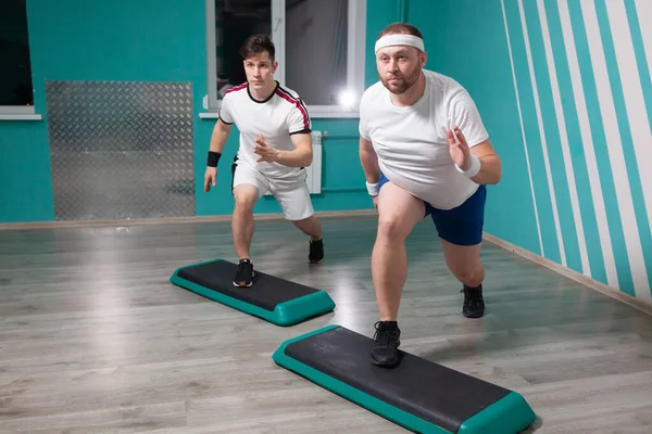 O homem gordo é muito trabalhador fazendo exercícios intensivos em etapas durante as aulas de fitness em grupo. Peso em excesso — Fotografia de Stock