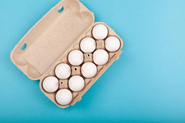 Eieren Kippeneieren. Bovenaanzicht van een open grijze doos met witte eieren. Geïsoleerd op een blauwe achtergrond. Het concept van een gezonde levensstijl, het krijgen van pure eiwitten. Goed ontbijt. Voorbereiding van Pasen. — Stockfoto